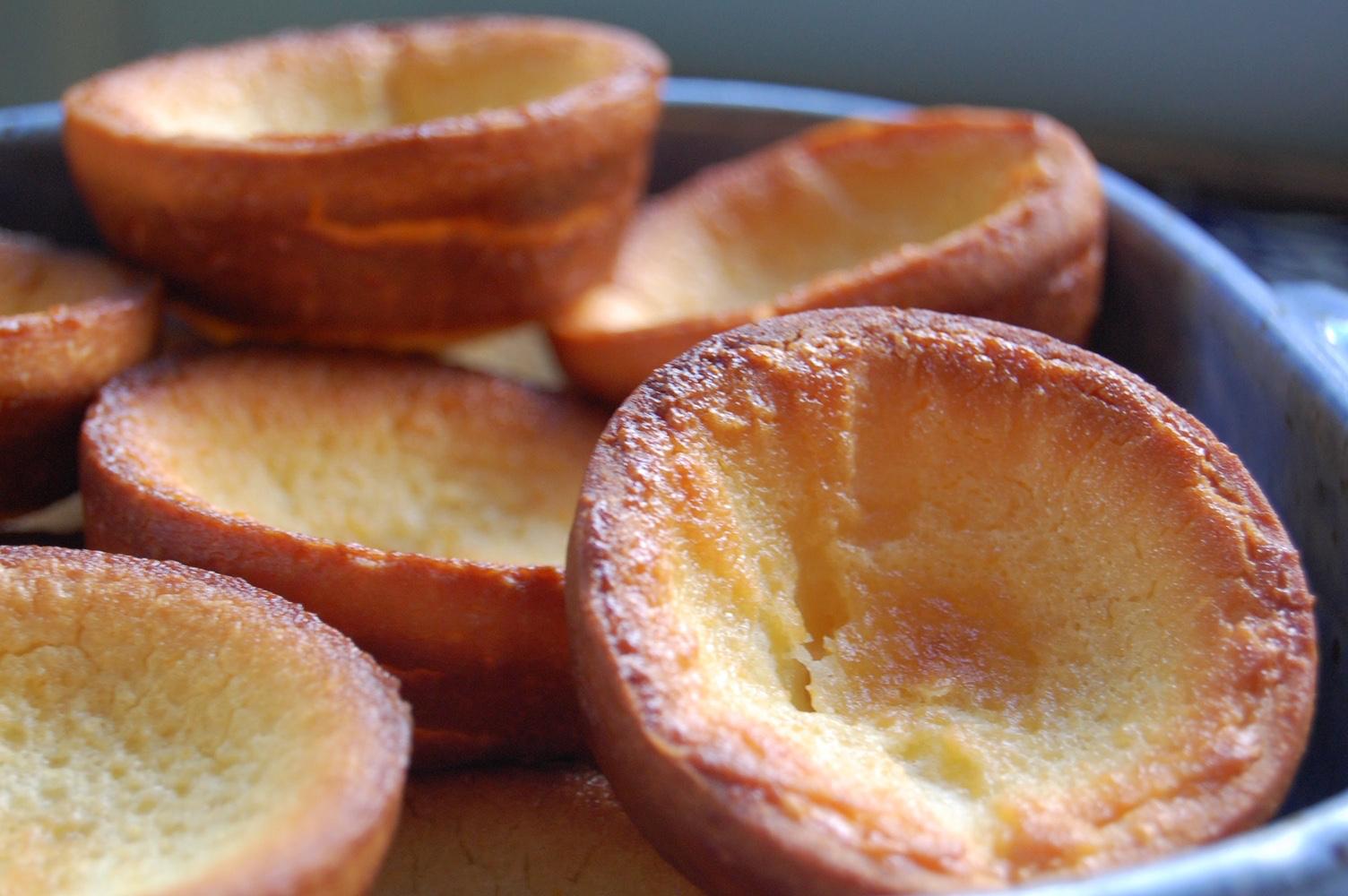 Close-up of several golden-brown milk tarts in a baking tray, showing their crisp, hollow centers and slightly uneven edges.