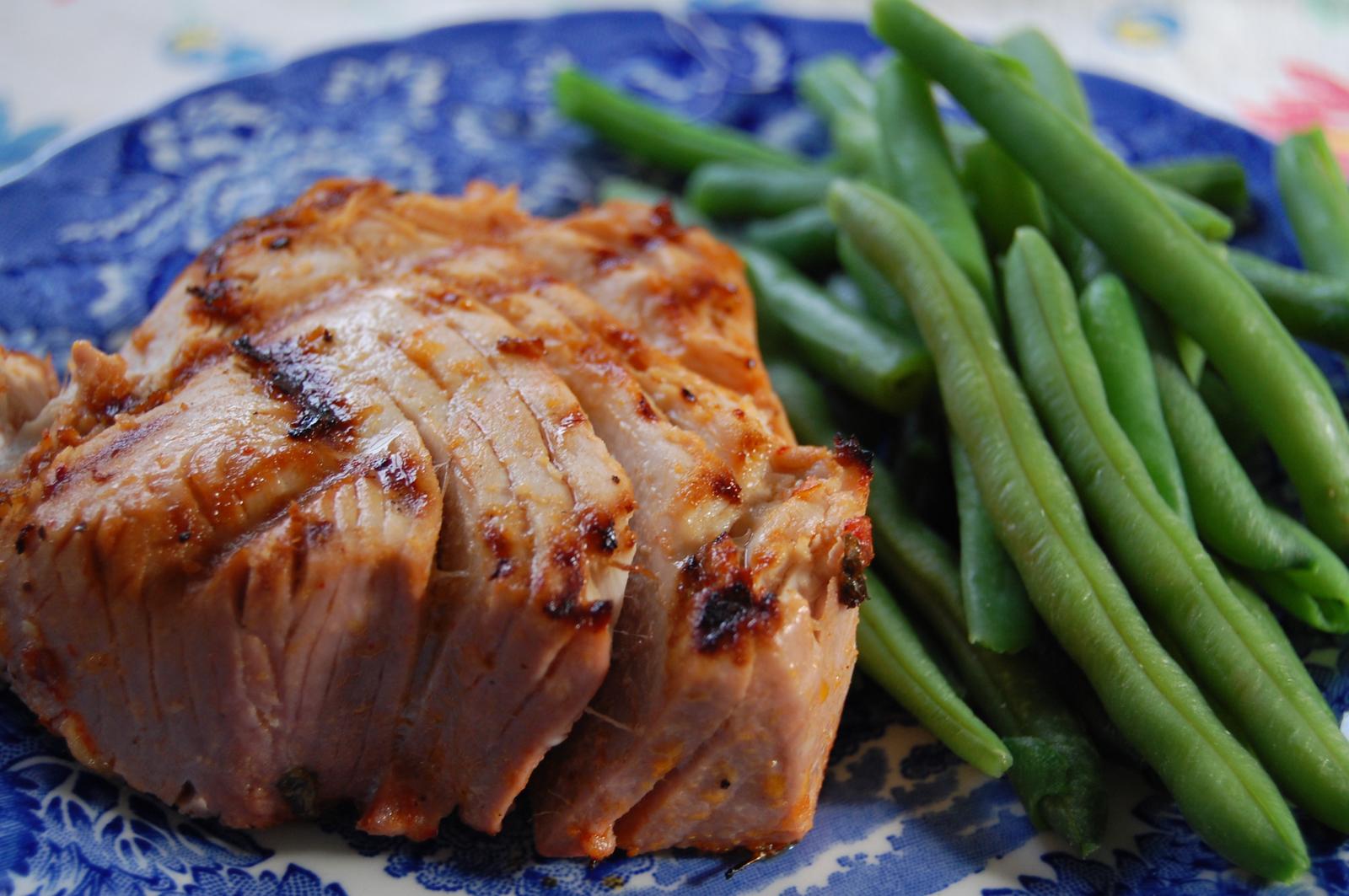 A grilled piece of tuna steak sits on a blue patterned plate next to a serving of cooked green beans.
